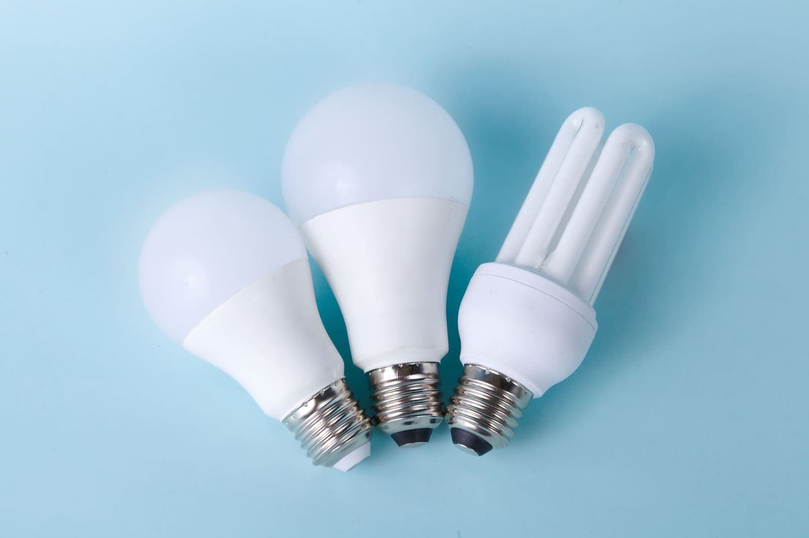 Twee ledlampen en een spaarlamp naast elkaar op een lichtblauwe ondergrond