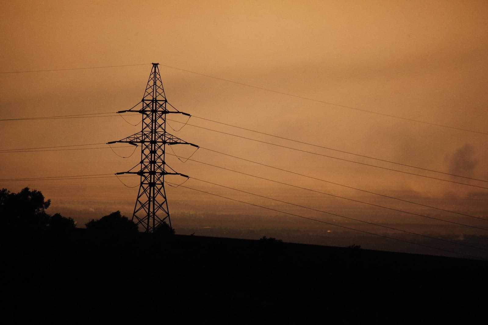 Hoogspanningsmast als silhouet tegen een oranje avondlucht
