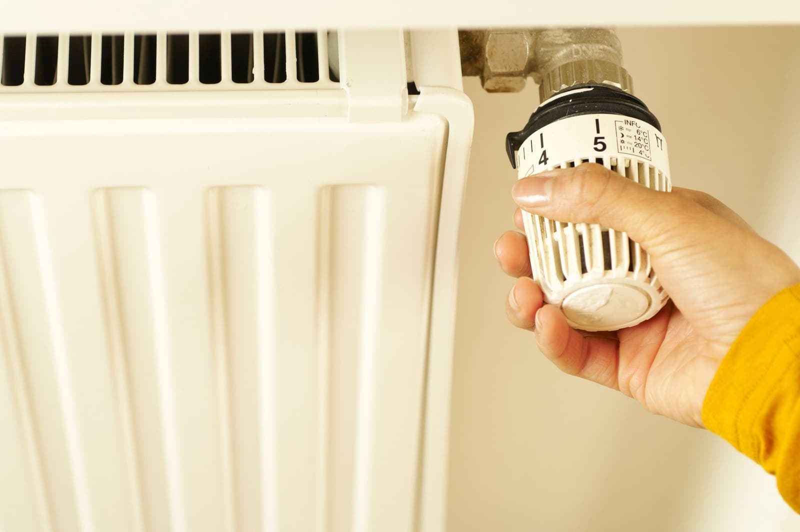 Hand die de thermostaatknop van een radiator lager draait